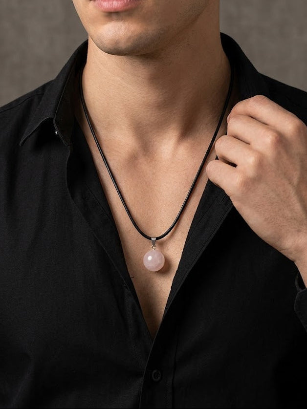 Man wearing a black shirt with a necklace featuring a pink pendant against a neutral background
