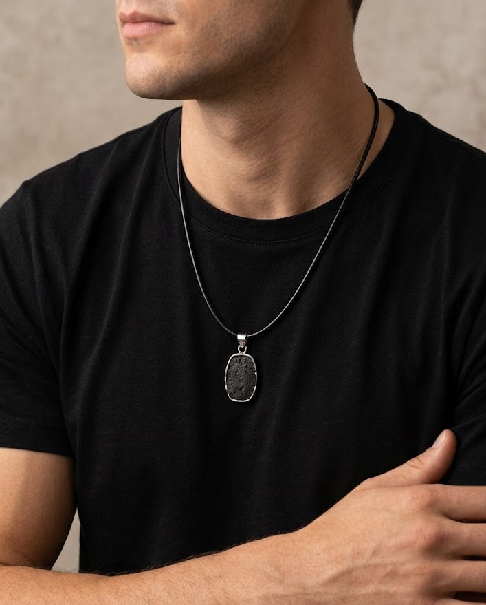 Man wearing a black t-shirt with a silver necklace and ring on a neutral background