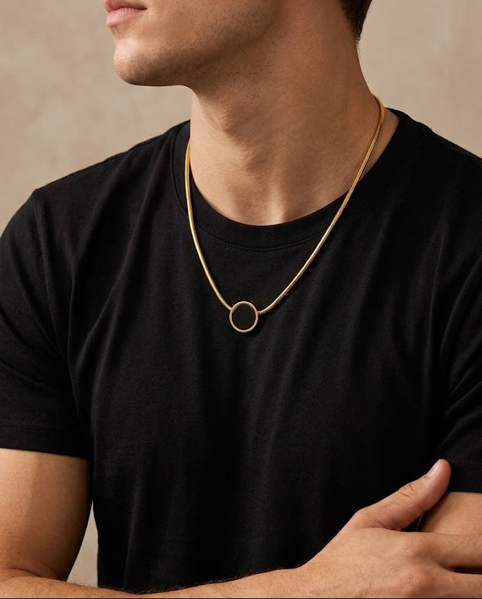 Man wearing a black t-shirt and gold necklace against a beige background