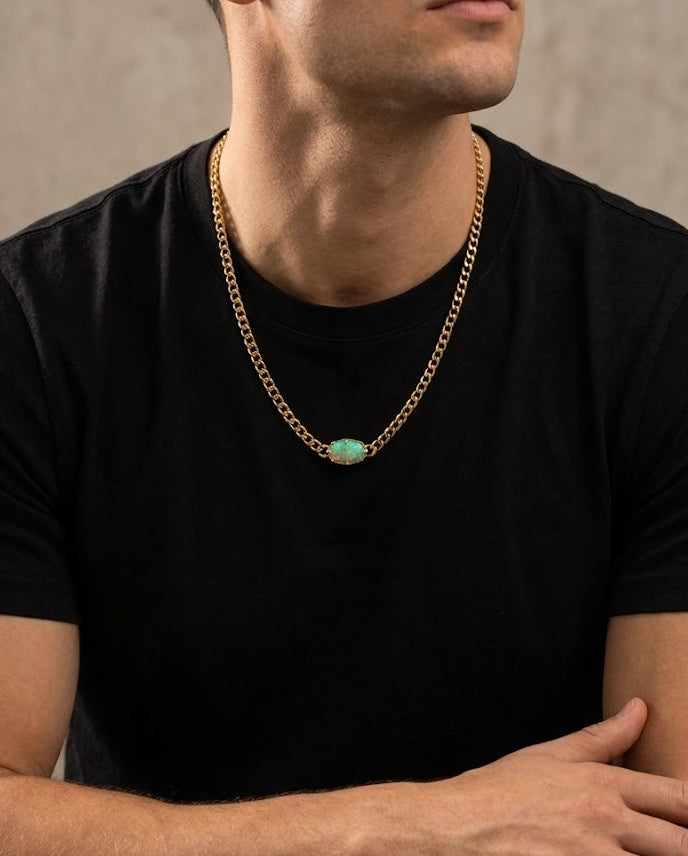 Man wearing a black t-shirt and gold chain necklace with a green pendant against a beige background