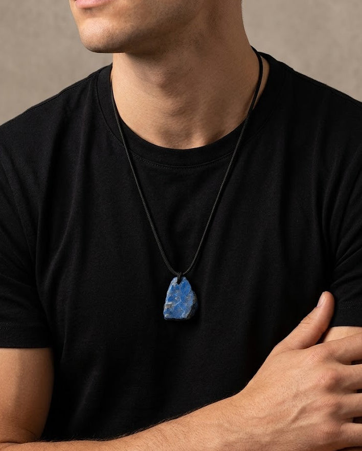 Man wearing a black t-shirt with a blue pendant necklace against a neutral background