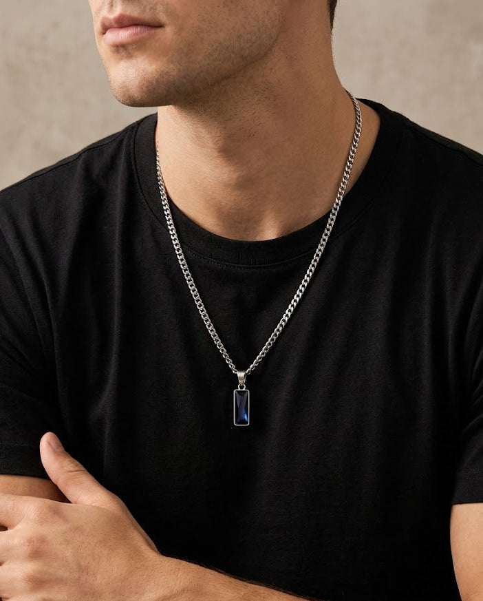 Man wearing a black t-shirt with a silver chain necklace featuring a blue pendant.