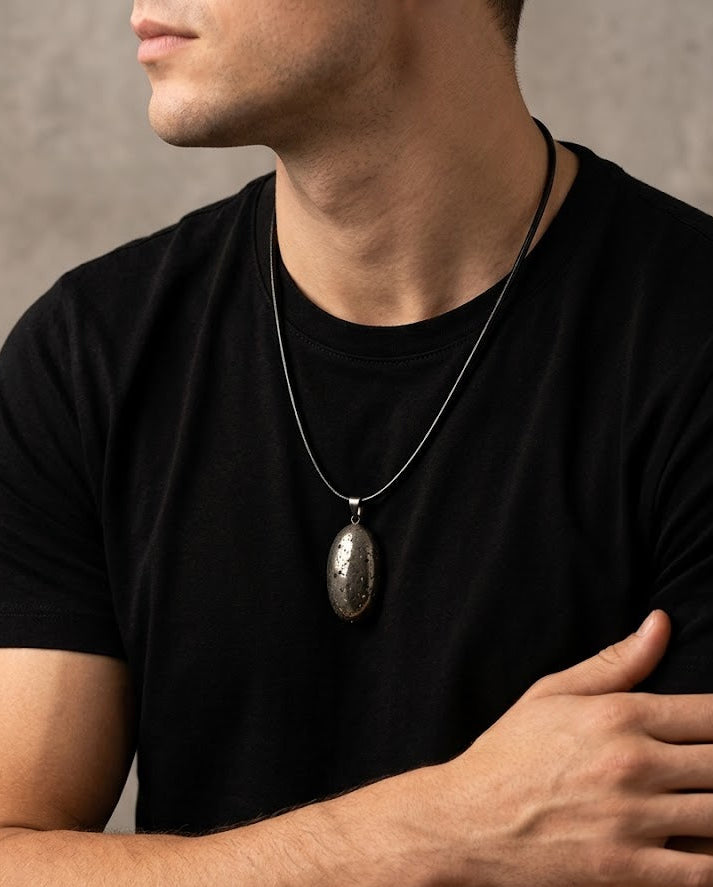 Man wearing a black t-shirt with a necklace featuring a large pendant against a neutral background
