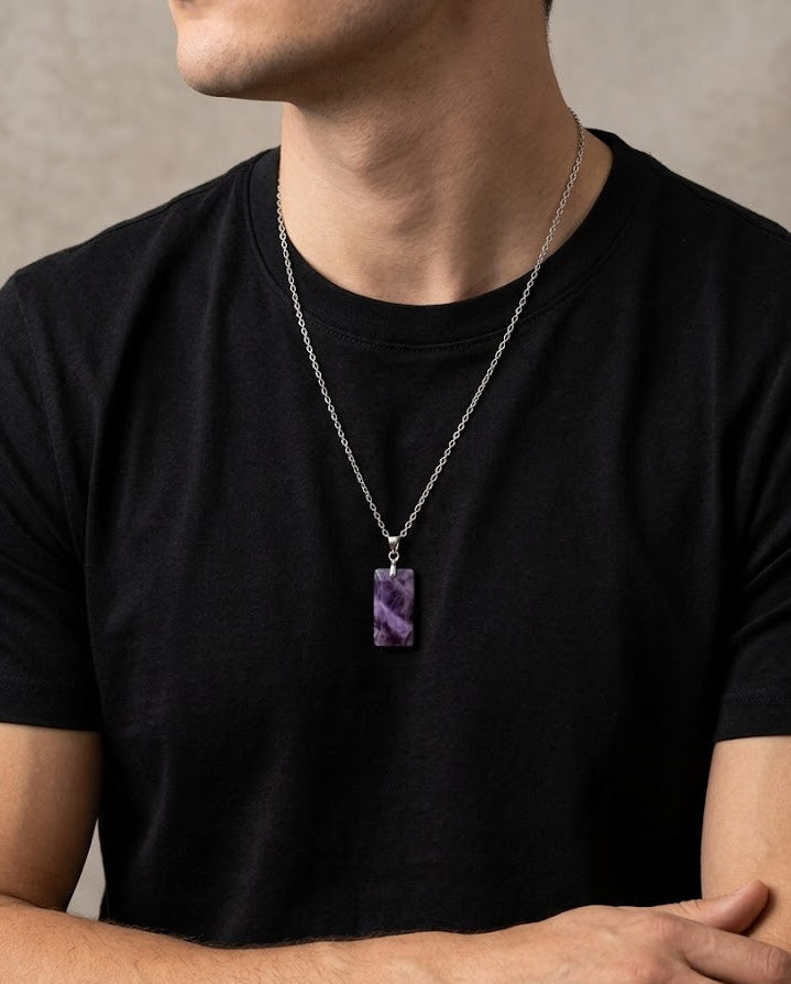 Man wearing a black t-shirt with a silver necklace featuring a purple pendant.