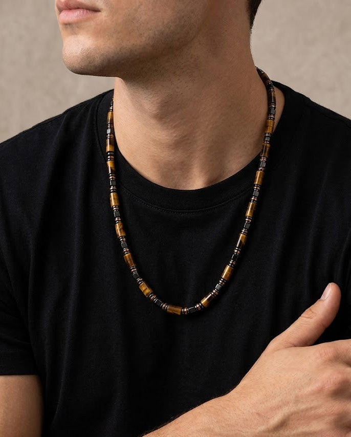 Man wearing a black t-shirt with a beaded necklace, against a neutral background