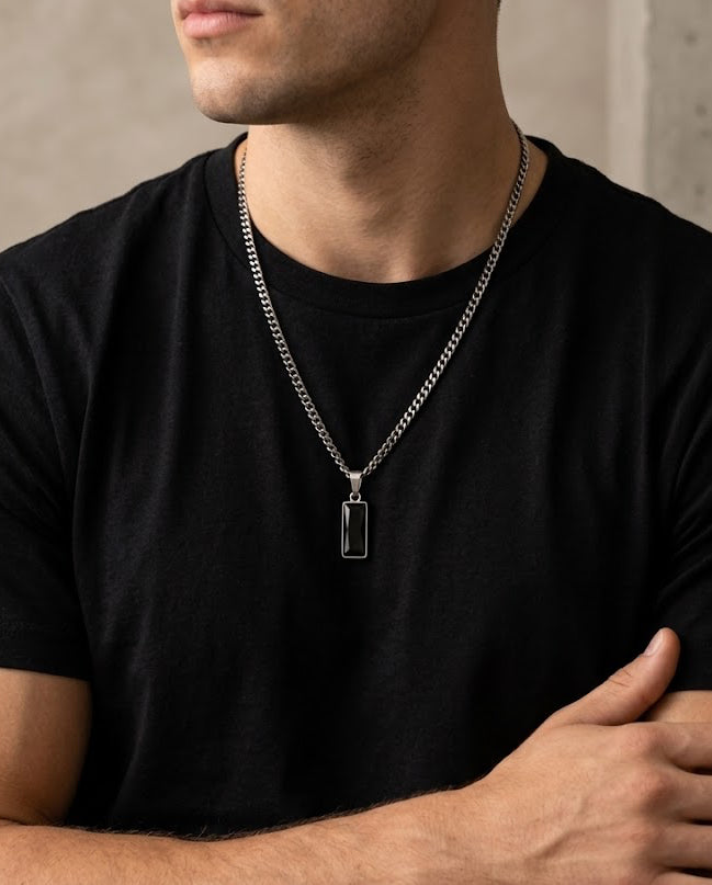 Man wearing a black t-shirt and silver necklace with a rectangular pendant.