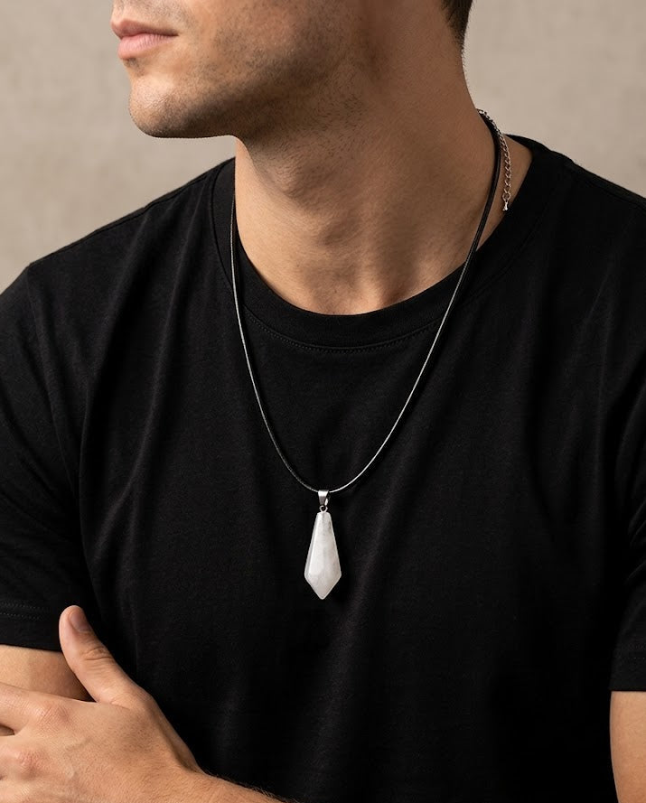 Man wearing a black t-shirt with a necklace featuring a white pendant against a neutral background