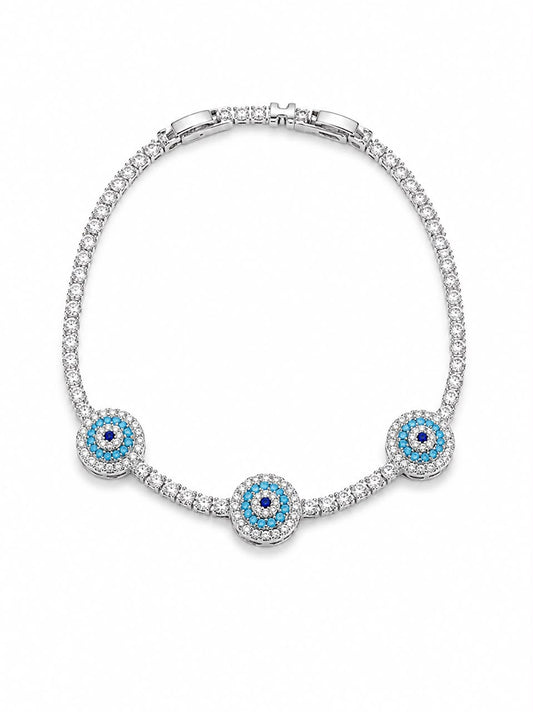 A silver-toned tennis bracelet featuring three circular evil eye motifs with light blue and dark blue stones, set with clear pavé diamonds on a white background.