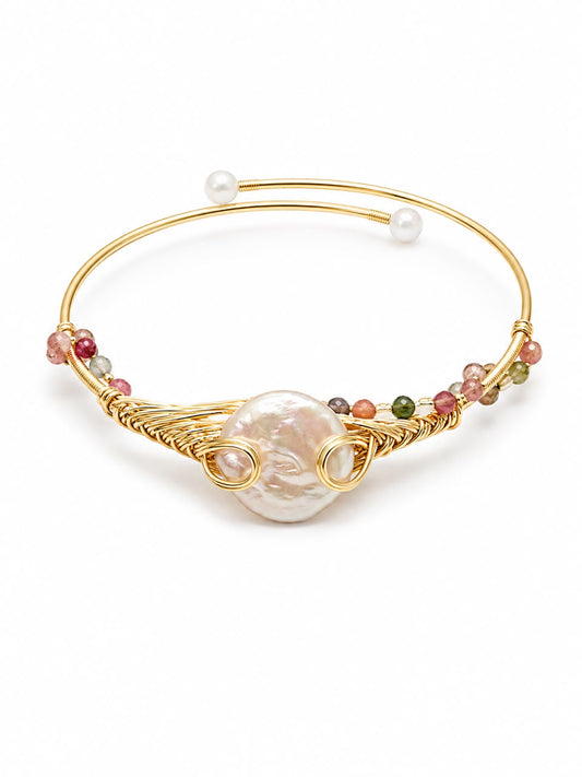 A gold-plated bangle bracelet featuring a large, organic-shaped white pearl at the center, accented by small multicolored beads and two smaller white pearls at the ends, set against a plain white background.