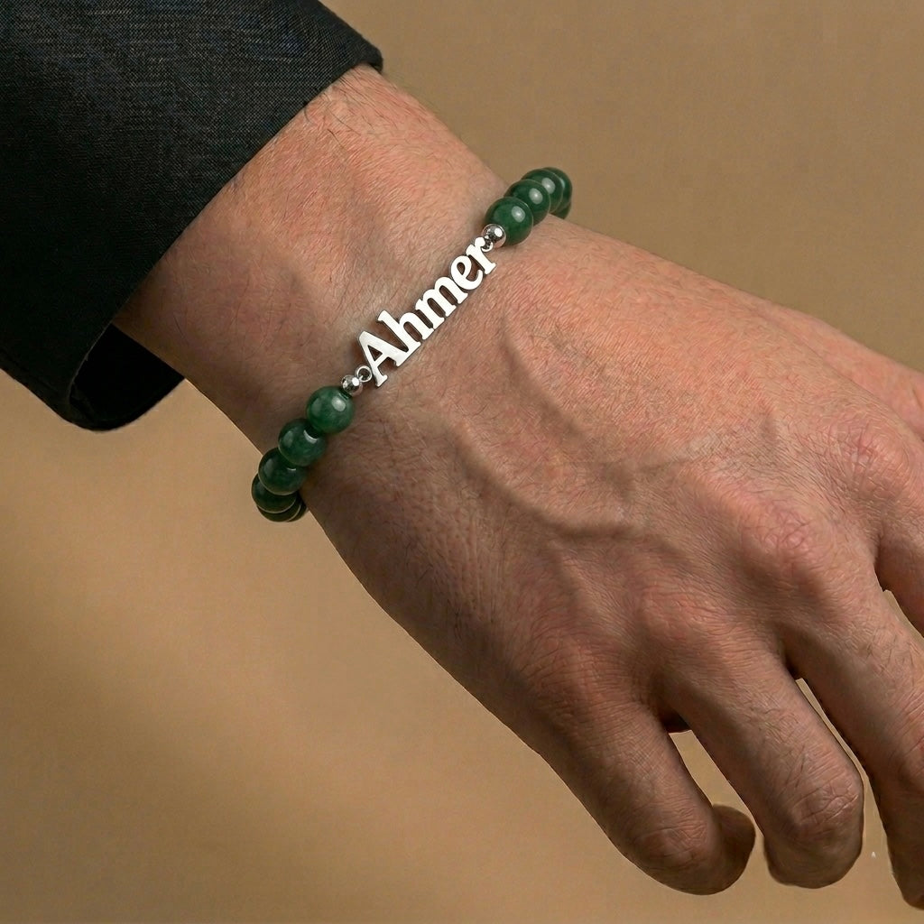 Green beaded bracelet with a silver charm on a wrist against a beige background