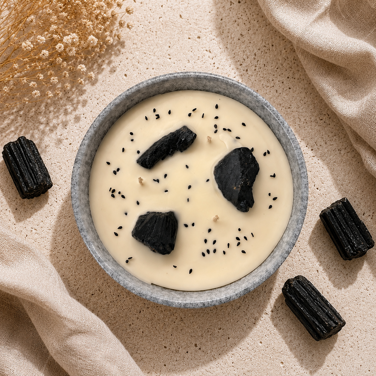 Bowl of creamy dessert with black sesame seeds and dark chocolate pieces on a beige surface.