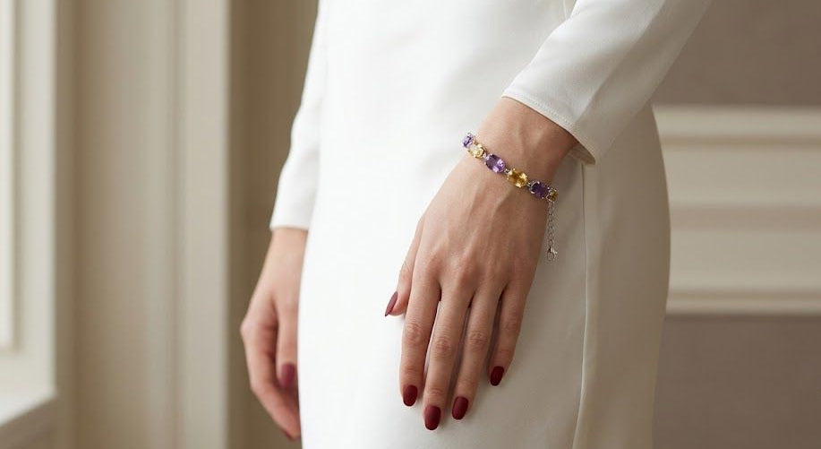 A close-up of a person wearing a delicate beaded bracelet with purple, yellow, and blue beads, styled on a white long-sleeve dress.