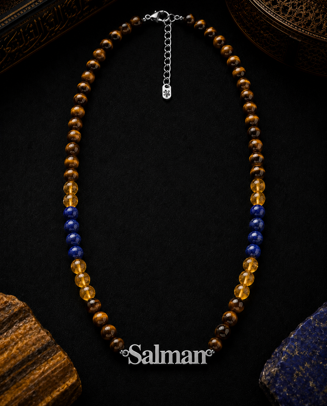 Necklace with brown, blue, and yellow beads on a dark surface with 'Salman' branding.