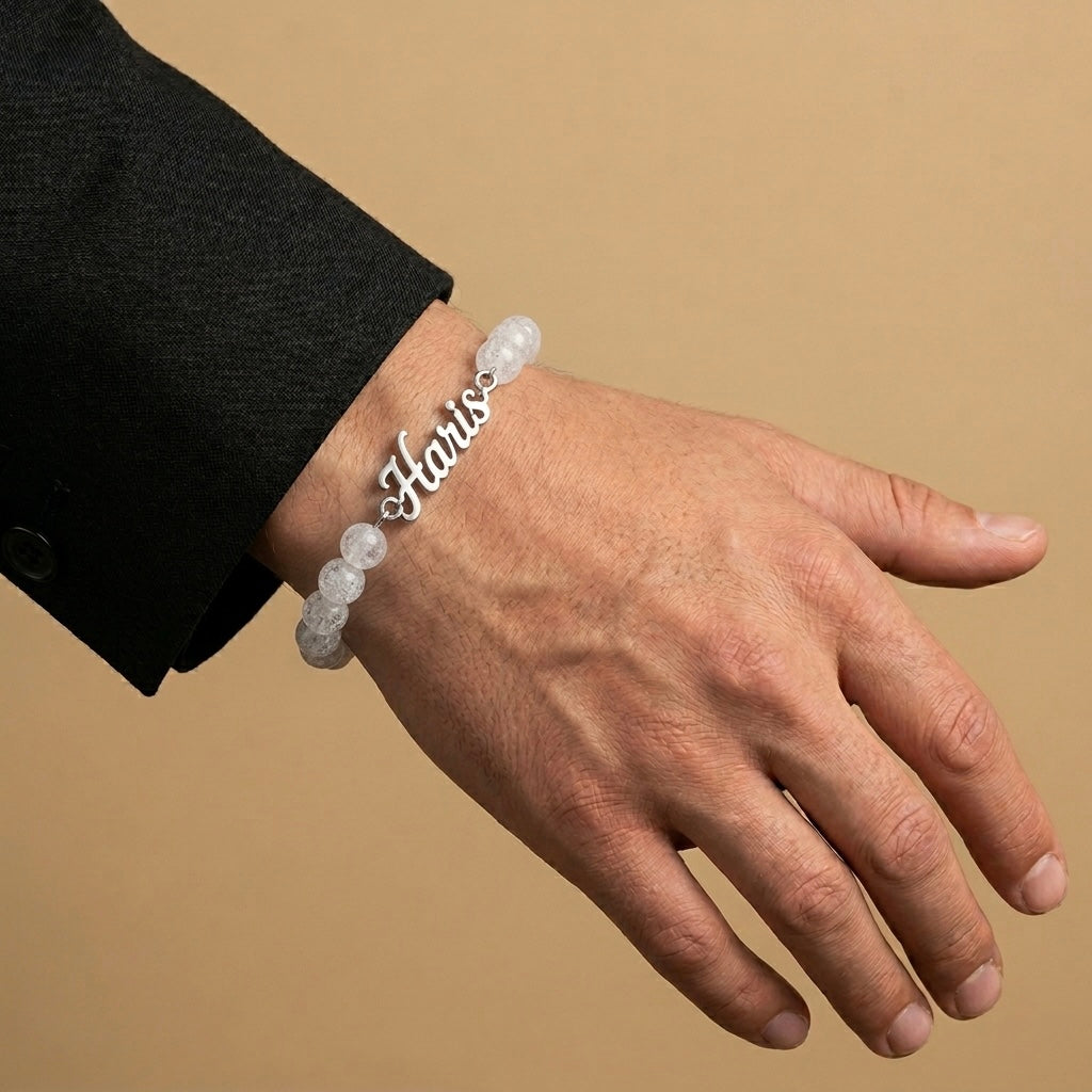 Hand wearing a bracelet with 'Haris' on a beige background