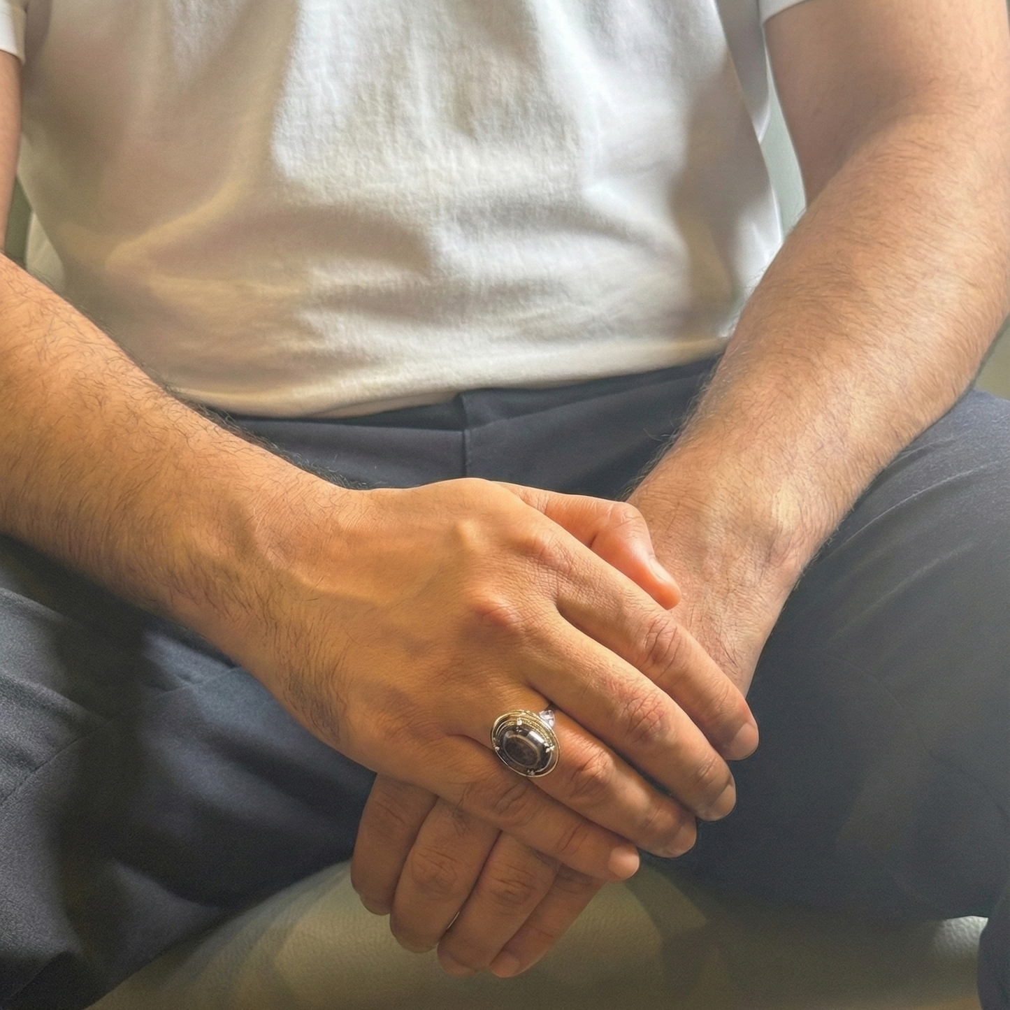 Person wearing a white shirt and dark pants sitting on a chair with hands clasped together.